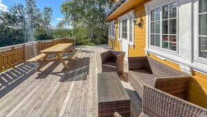 A wooden deck with picnic tables and wicker chairs, overlooking a forested area. - Lovely home in Lindesnes with sauna (Lindesnes)