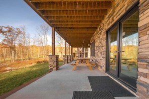 A covered patio with a stone wall, wooden beams, and a picnic table.