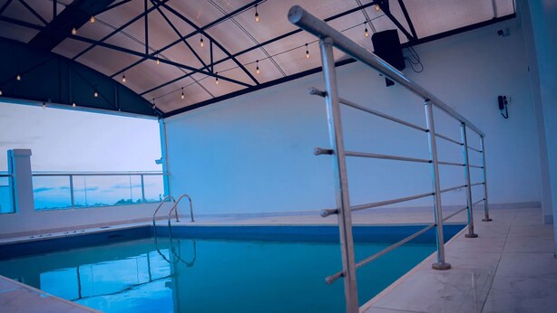 An indoor swimming pool with a metal ladder and a view of the sea through large windows. - HomeWorth Hotel (Lekki)