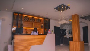 A reception area with a wooden reception desk, a chandelier, and a sign indicating a 'squad' service. - HomeWorth Hotel (Lekki)