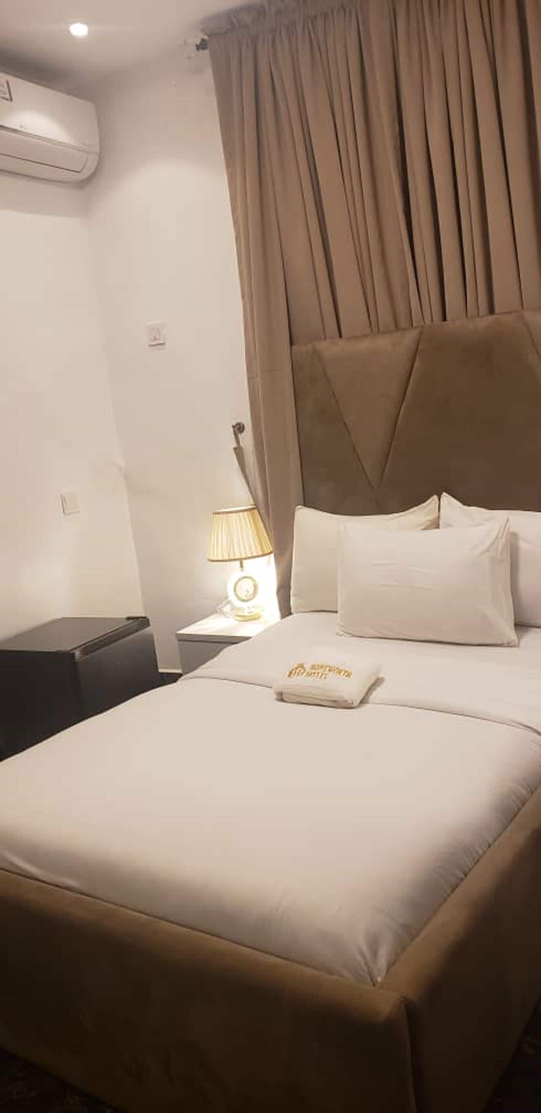 A hotel room with a bed, a nightstand with a lamp, and an air conditioning unit on the wall.