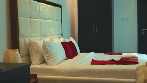 A neatly made bed with white and red bedding, a wooden headboard, and a lamp on a bedside table. - HomeWorth Hotel (Lekki)