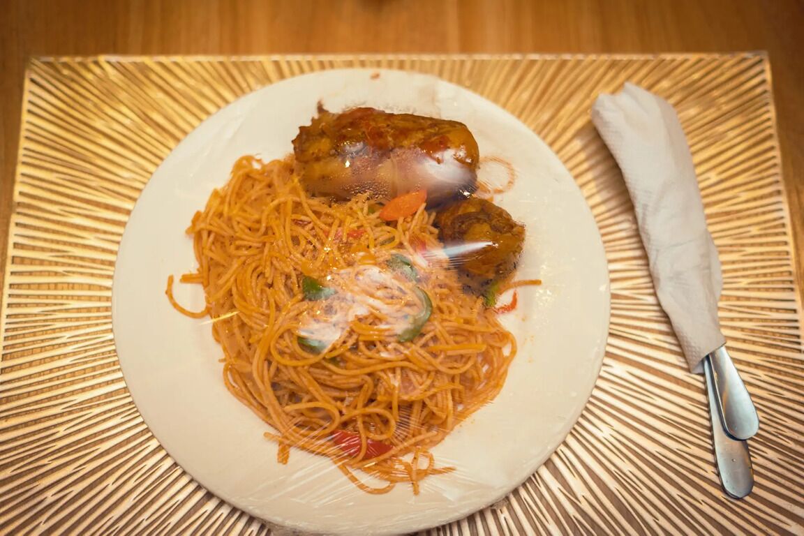 A plate of noodles with vegetables and a piece of meat on a white plate.