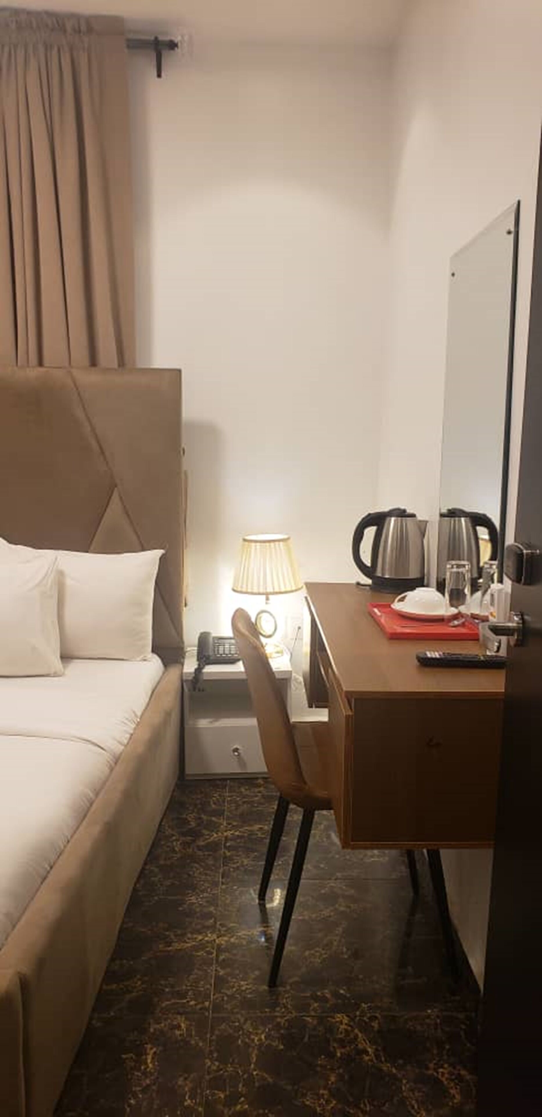 Habitación de hotel con cama, escritorio, silla, lámpara, cafetera y espejo.
