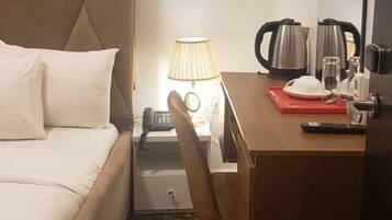 Habitación de hotel con cama, escritorio, silla, lámpara, cafetera y espejo.