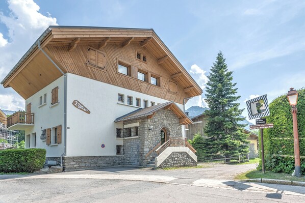 A two-story building with a stone facade and wooden upper levels, featuring a staircase and a balcony.