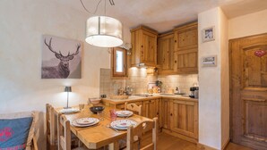 A cozy kitchen with wooden cabinets, a dining table set for four, and a pendant light. - Studio Montée du Calvaire - Welkeys (Megève)