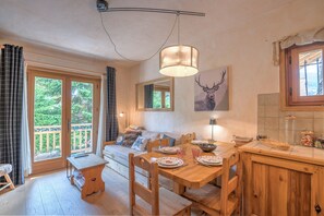 A cozy dining area with a wooden table and chairs, a bench, and a sofa. There is a large window with curtains, a ceiling light, and a wall-mounted picture of a deer.