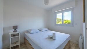 A bedroom with a bed, a bedside table with a lamp, a window, and a radiator. - Appartement des Martrois - Welkeys (Villers-sur-Mer)