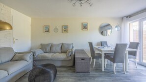 A living room with a sofa, ottoman, dining table, chairs, and a small basket. - Appartement des Martrois - Welkeys (Villers-sur-Mer)