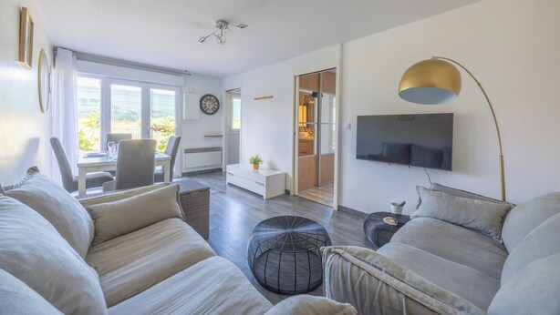 A modern living room with a sofa, ottoman, and a TV mounted on the wall. - Appartement des Martrois - Welkeys (Villers-sur-Mer)
