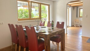 A dining area with a wooden table and red chairs, large windows with a view of greenery, and a cross on the wall. - Panoramablick by Interhome (Reutte)