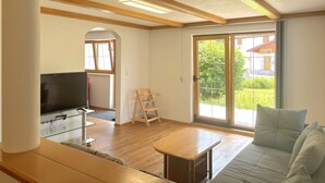 A living room with a TV, wooden furniture, a sofa, and a sliding glass door leading to a garden. - Panoramablick by Interhome (Reutte)