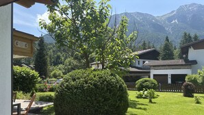 A courtyard with a large tree, a patio with chairs, and a mountain backdrop. - Panoramablick by Interhome (Reutte)