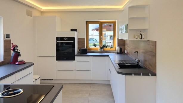 A modern kitchen with white cabinetry, a built-in oven, a coffee machine, and a window with a view of the outside. - Panoramablick by Interhome (Reutte)