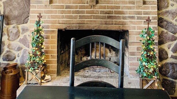 Una chimenea de piedra con repisa, dos pequeños árboles de Navidad y una mesa al frente.
