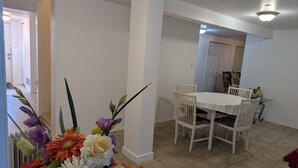 Un comedor con una mesa y sillas blancas, un jarrón de flores y una puerta al fondo.