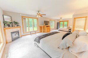 A spacious bedroom with a large bed, a wooden dresser, a TV, and a fireplace. - Lost in the Woods: Pictured Rocks Fall Getaway | ORV Trails | Sleeps 10 (Munising)