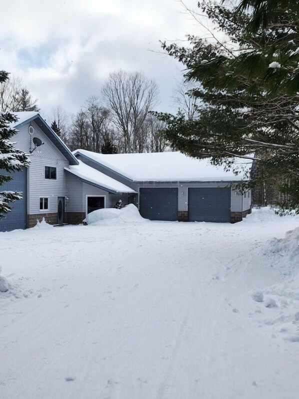 A two-story house with a garage and a driveway covered in snow. - Lost in the Woods: Pictured Rocks Fall Getaway | ORV Trails | Sleeps 10 (Munising)