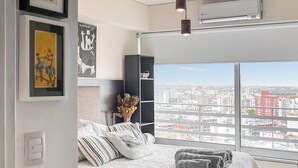 A modern bedroom with a large bed, city view, air conditioning, and artwork on the wall.
