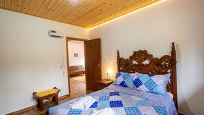 A bedroom with a wooden headboard, a bed with a blue and white quilt, a bedside table with a lamp, and a bench by the door. - Refugio Jaguary Country House (Monte Verde)