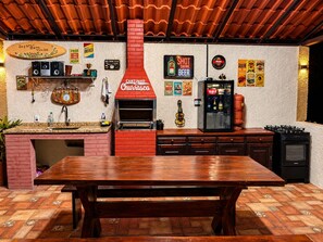 A kitchen with a brick wall, a wooden table, a red chimney, and various kitchen appliances. - Refugio Jaguary Country House (Monte Verde)