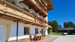 A traditional chalet with a stone foundation, wooden balconies with flower boxes, and a paved patio area with outdoor seating. - Berganger by Interhome (Wildschönau)