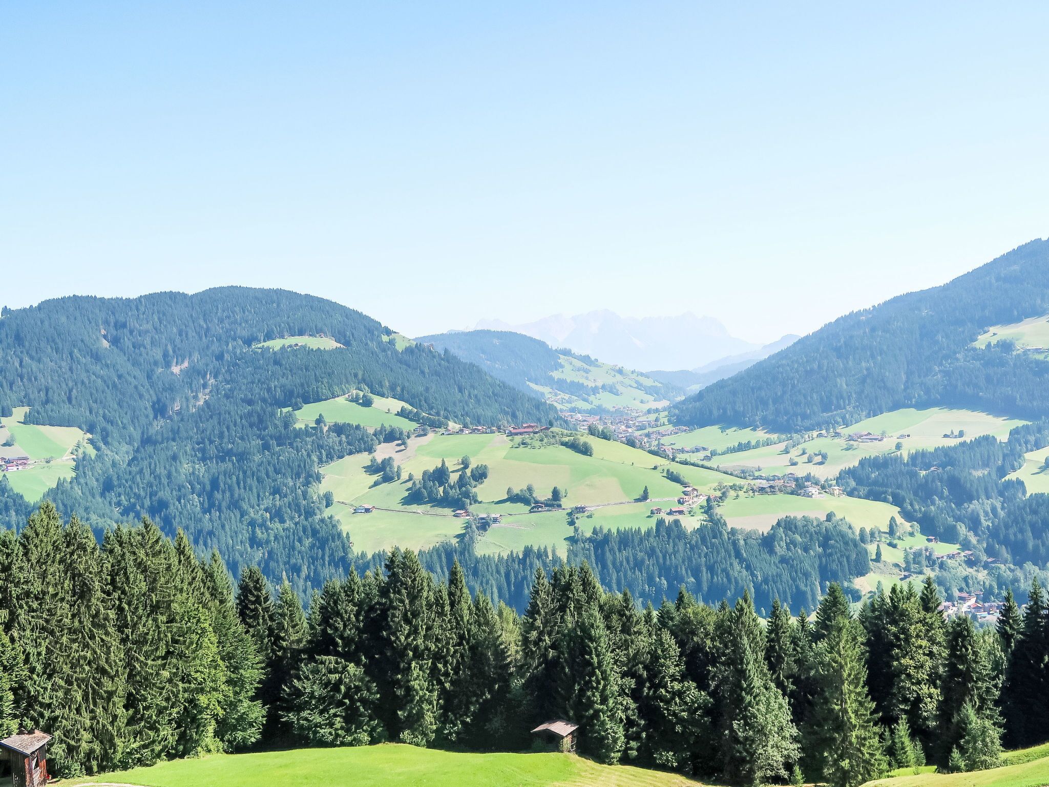 Ein weiter Panoramablick auf eine gebirgige Landschaft mit einem Tal, dichten Wäldern und verstreuten Gebäuden.