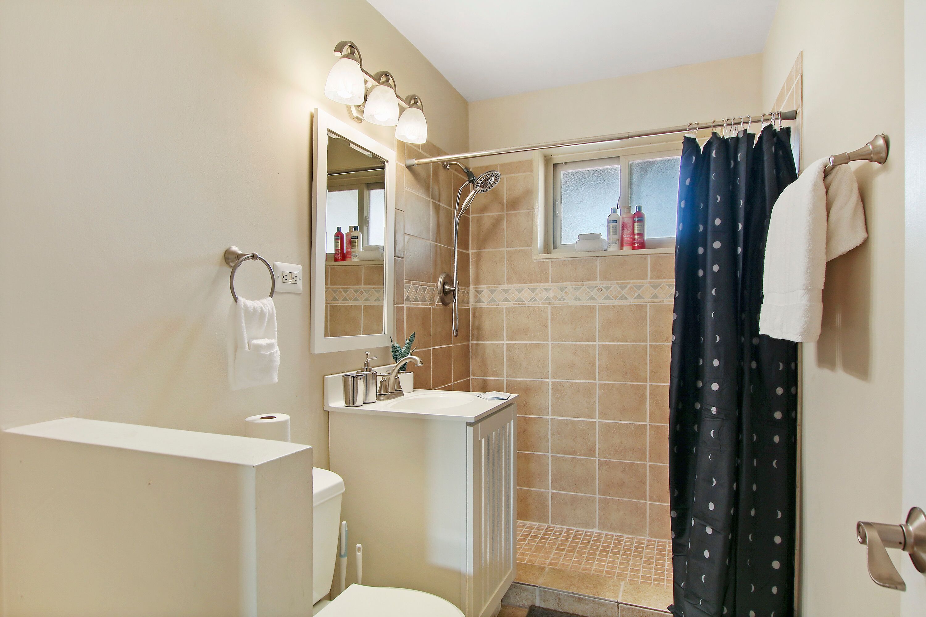 A bathroom with a shower, toilet, sink, and a mirror.