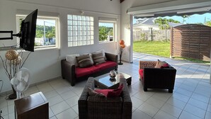 A spacious living area with a high ceiling, large windows, and a view of the outdoors. - Maison Sainte-anne (Sainte-Anne)