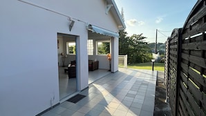 A covered outdoor area with tiled flooring, a white building, and a wooden fence. - Maison Sainte-anne (Sainte-Anne)