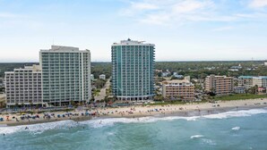 A coastal hotel with multiple floors, a beach in the foreground, and a clear sky. - Oceans One 908 (Myrtle Beach)