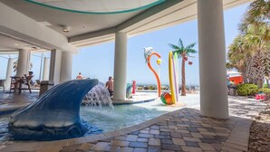 A water feature with a dolphin sculpture, palm trees, and a pool area. - Oceans One 908 (Myrtle Beach)