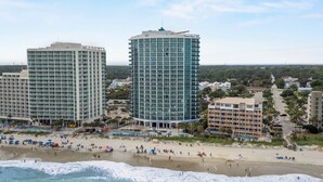A coastal hotel with multiple floors, a beach in the foreground, and surrounding buildings. - Oceans One 908 (Myrtle Beach)