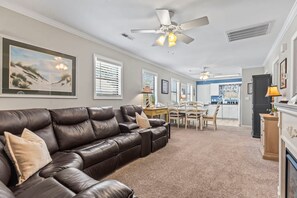 A living room with a leather sofa, ceiling fans, a dining area with a table and chairs, and a kitchen in the background.