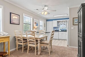 A dining area with a table and chairs, a ceiling fan, and a kitchen in the background.
