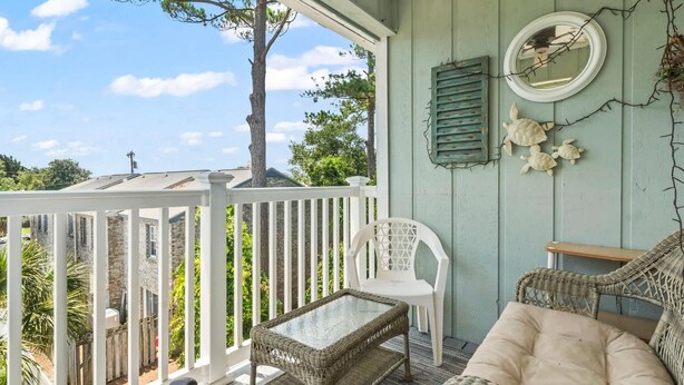 Une véranda avec des meubles en osier, une chaise blanche et une table en verre.