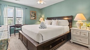 Une chambre à coucher avec un lit, des tables de chevet, un ventilateur de plafond et une fenêtre avec des rideaux.