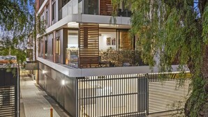 Un immeuble moderne à deux étages, doté de grandes fenêtres, d’un balcon et d’une entrée sécurisée par un portail.
