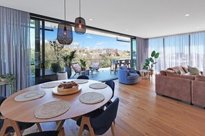Una sala de estar moderna con un gran ventanal que da a un patio, una mesa de comedor redonda con individuales y un sofá con cojines.