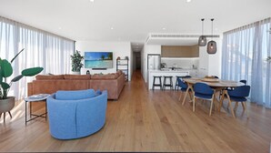 Un salon moderne avec un canapé marron, un fauteuil bleu et un coin repas comprenant une table en bois et des chaises bleues.