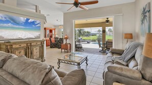 A spacious living room with a large flat-screen TV, comfortable seating, a ceiling fan, and a view of a pool and outdoor area. - Rotonda West Private Pool Vacation Home On Canal (Rotonda West)