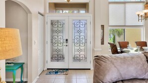 A well-lit entrance with a frosted glass door, a dining area with chairs and a table, and a chandelier. - Rotonda West Private Pool Vacation Home On Canal (Rotonda West)