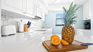 A modern kitchen with white cabinets, a tiled backsplash, and a pineapple on a cutting board. - Direct Oceanfront Condo w/ Pool, Private Balcony & Ocean-View Master Bedroom (Cape Canaveral)