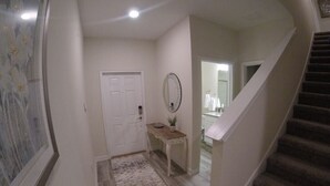 Un pasillo con una puerta, una pequeña mesa con espejo y una escalera que lleva a otra habitación.