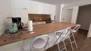 A modern kitchen with white cabinets, a wooden countertop, and a built-in stove. There are three white bar stools and a metal coffee table with a paper towel holder.
