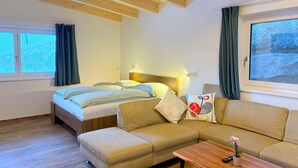 A cozy room with a bed, a sofa, a wooden coffee table, and a window with curtains.