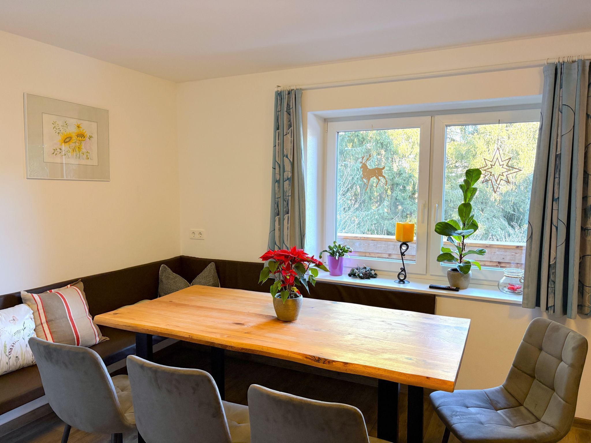 A dining area with a wooden table, four chairs, a bench with cushions, a potted plant, a wall-mounted lamp, and a window with curtains.