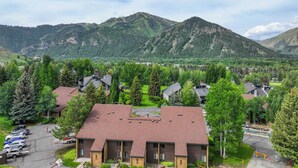 A residential area with houses surrounded by mountains, featuring a central building with a red roof and a parking area. - Bigwood Basecamp with Mountain Views & Great Location (Ketchum)