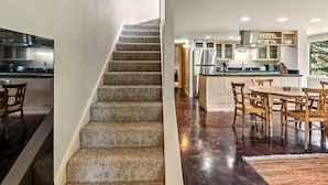 A modern kitchen with a central island, wooden chairs, and a staircase. - Bigwood Basecamp with Mountain Views & Great Location (Ketchum)